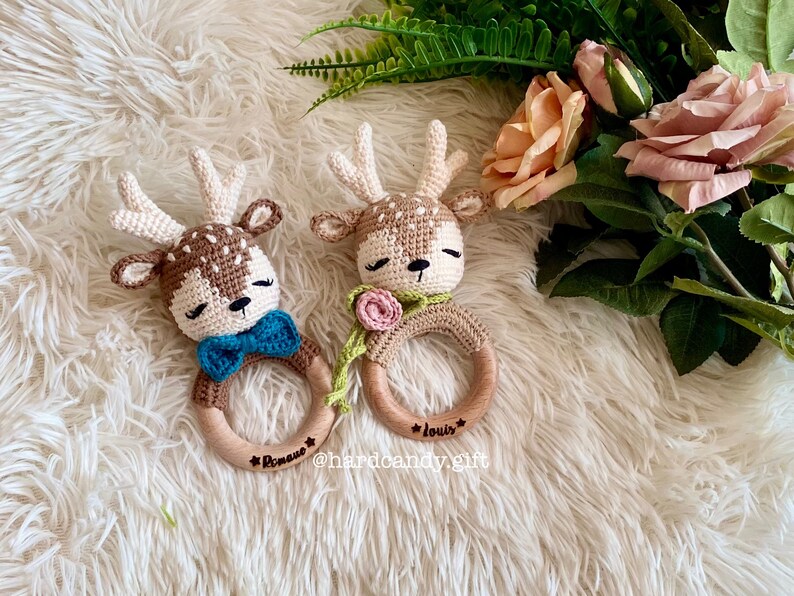 May include: Two crocheted deer rattle toys with wooden rings. The rings are engraved with the names "Roman" and "Louis".