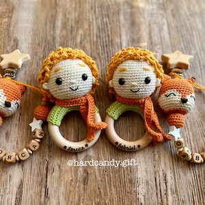 May include: Two handmade crochet baby teethers. Each teether features a Little Prince doll with orange hair and scarf, a fox, and wooden beads spelling out a name. The teethers are attached to a wooden ring.