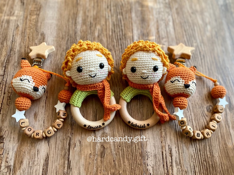 May include: Two handmade crochet baby teethers. Each teether features a Little Prince doll with orange hair and scarf, a fox, and wooden beads spelling out a name. The teethers are attached to a wooden ring.