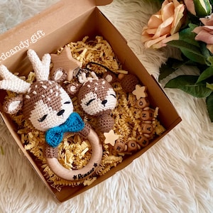 May include: A gift box filled with brown and white crocheted deer toys, a wooden star, and wooden letter blocks that spell "Romeo". The box is lined with brown shredded paper.