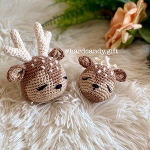 May include: Two crocheted deer plushies with brown and white fur, closed eyes, and black noses. The deer are lying on a white fluffy surface. The text "@hardcandy.gift" is visible in the background.