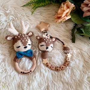 May include: A brown crocheted deer rattle with a blue bow tie and the name "Roman" engraved on the wooden ring. A matching crocheted deer with a wooden star and beads with the name "Roman" spelled out.