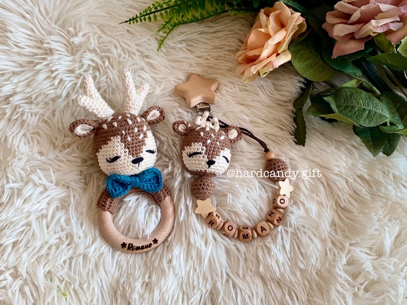 May include: A brown crocheted deer rattle with a blue bow tie and the name "Roman" engraved on the wooden ring. A matching crocheted deer with a wooden star and beads with the name "Roman" spelled out.