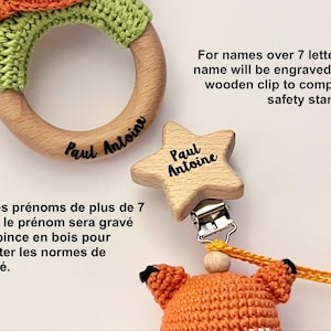 May include: A wooden teething ring with green crochet detail and the name Paul Antoine engraved, alongside a star-shaped wooden clip with the name Paul Antoine and a crocheted orange fox toy. Text states: For names over 7 letters, the name will be engraved on the wooden clip to comply with safety standards.