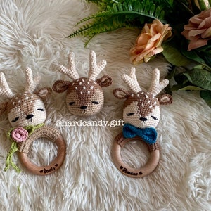 May include: Three crocheted deer head teethers with wooden rings. The teethers are brown and white with embroidered eyes and noses. The rings are engraved with the names "Louis", "Romano", and "*" .