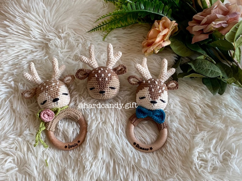 May include: Three crocheted deer head teethers with wooden rings. The teethers are brown and white with embroidered eyes and noses. The rings are engraved with the names "Louis", "Romano", and "*" .