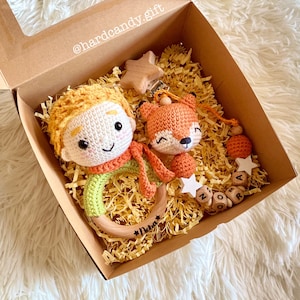 May include: A gift box containing a crocheted Little Prince doll with a wooden ring teether, a crocheted fox toy, and a pacifier clip with wooden beads. The box is filled with yellow paper shreds and includes wooden star accents.