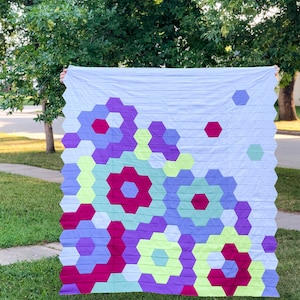 Puede incluir: Una colcha con un patr&oacute;n geom&eacute;trico de hex&aacute;gonos en tonos de morado, verde, amarillo y rojo. La colcha est&aacute; hecha con una tela de fondo azul claro.