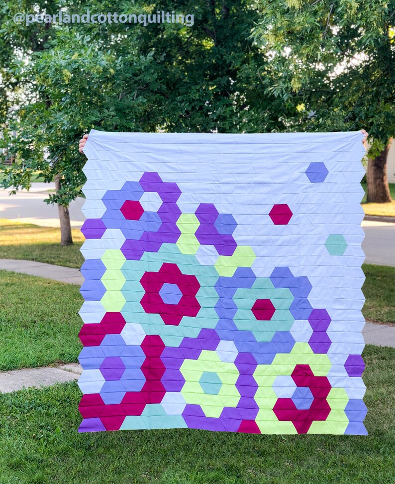 Puede incluir: Una colcha con un patr&oacute;n geom&eacute;trico de hex&aacute;gonos en tonos de morado, verde, amarillo y rojo. La colcha est&aacute; hecha con una tela de fondo azul claro.