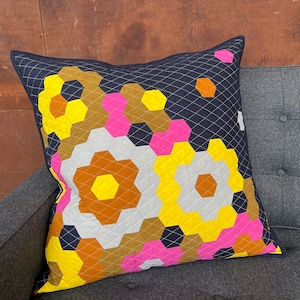 Puede incluir: Una almohada decorativa con un patr&oacute;n geom&eacute;trico en tonos de amarillo, rosa, marr&oacute;n y blanco sobre un fondo azul oscuro.