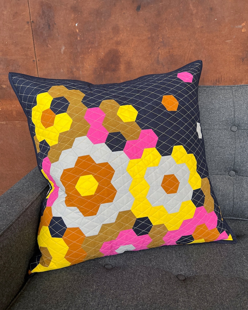 Puede incluir: Una almohada decorativa con un patr&oacute;n geom&eacute;trico en tonos de amarillo, rosa, marr&oacute;n y blanco sobre un fondo azul oscuro.