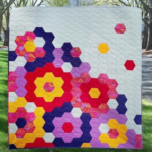 Puede incluir: Una colcha con un patr&oacute;n geom&eacute;trico de hex&aacute;gonos en tonos de rojo, amarillo, morado y blanco. Los hex&aacute;gonos est&aacute;n dispuestos en un patr&oacute;n en cascada, creando un dise&ntilde;o moderno y abstracto.