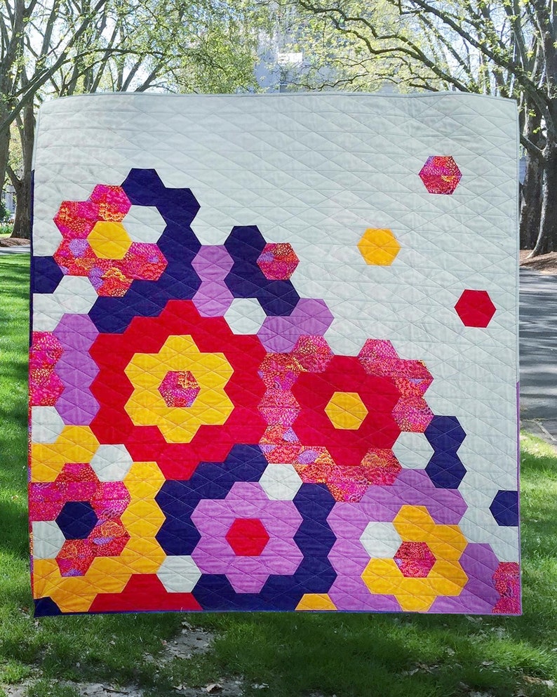 Puede incluir: Una colcha con un patr&oacute;n geom&eacute;trico de hex&aacute;gonos en tonos de rojo, amarillo, morado y blanco. Los hex&aacute;gonos est&aacute;n dispuestos en un patr&oacute;n en cascada, creando un dise&ntilde;o moderno y abstracto.