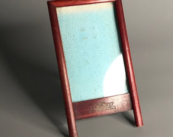 May include: A dark wood picture frame with a light blue mat and a stand on the back. The frame is empty.