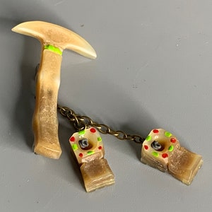 May include: A set of three vintage-style, beige-colored, ice pick-shaped, metal and plastic, novelty pins. The pins are connected by a gold chain. The ice pick has a green and red painted design. The two smaller pins have a red and green painted design.