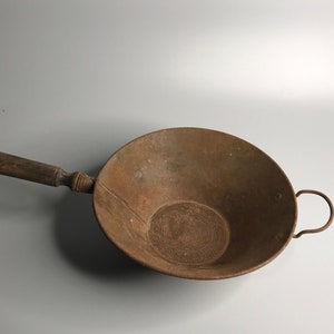 Op de afbeelding: Een roestige metalen zeef met een houten handvat. De zeef heeft een gaasbodem en een afgeronde komvorm.