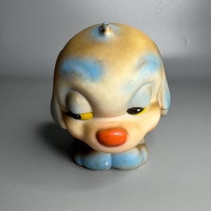 Könnte beinhalten: Vintage Hunde-Figur mit einem skurrilen Design. Der Hund hat einen cremefarbenen Körper mit blauen und braunen Akzenten. Er hat eine rote Nase, schwarze Augen und gelbe Akzente um die Augen. Die Figur ist ein Sammlerstück.