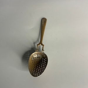 Puede incluir: Un infusor de té de plata vintage con un cuenco perforado y un mango largo.