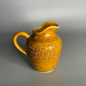 Op de afbeelding: Een bruine keramische kan met een gestreept ontwerp en de tekst "DOMAINE de TRIFUNA PALAVESE PORTO-VECCHIO" aan de zijkant.