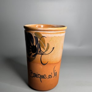 Può includere: Una tazza in ceramica marrone con un motivo floreale nero e marrone e il testo "Brique a la" sul lato.