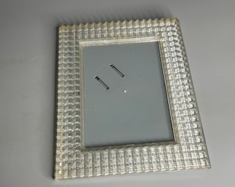 May include: A white plastic picture frame with a textured border. The frame has two slots for holding a picture.