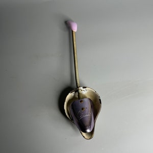 May include: A vintage metal shoe stretcher with a spring-loaded handle and a pink plastic tip. The stretcher is designed to help maintain the shape of shoes and prevent wrinkles. The stretcher has the word "Cudas" printed on it.