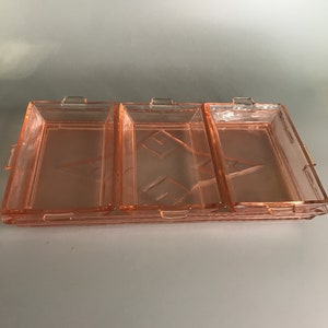 Puede incluir: Un juego de tres platos de servir de vidrio rosa con un patrón decorativo. Los platos son rectangulares y tienen un borde elevado. Son perfectos para servir aperitivos, aperitivos o postres.