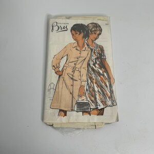 Könnte beinhalten: Vintage-Schnittmuster für ein Kleid mit Gürteltaille und langen Ärmeln. Das Schnittmuster ist für die Größen 10-18 und stammt von der Marke 'Butterick'.