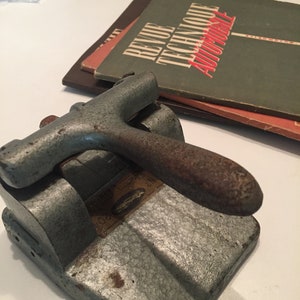 Könnte beinhalten: Ein alter, grauer Papierlocher aus Metall mit einem rostigen Griff. Der Locher hat ein Etikett mit der Aufschrift "No. 80".