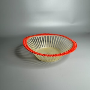 May include: A white plastic bowl with a red rim. The bowl has a woven design and is perfect for serving fruit or snacks.