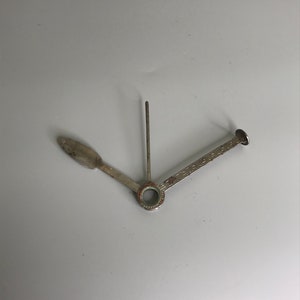 Puede incluir: Una herramienta de metal plateado para pipa con un tallo largo y delgado y un tazón pequeño y redondo. La herramienta está diseñada para empacar y limpiar pipas.