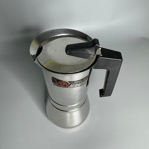 Può includere: Una macchina per caffè espresso in acciaio inox con manico nero e logo VeV. La macchina ha un coperchio rotondo argentato con un pomello nero.
