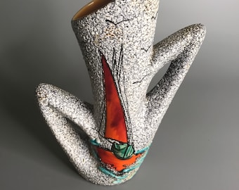 Puede incluir: Un jarrón de cerámica blanca con una superficie texturizada y un diseño abstracto pintado en naranja, rojo y azul. El jarrón tiene la forma de una persona sentada con las piernas cruzadas.