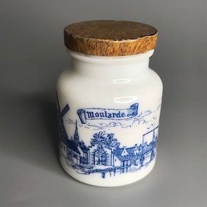 Könnte beinhalten: Weiße Keramikdose mit einem Holzdeckel und einer blauen und weißen Illustration einer Windmühle und einer Stadt mit dem Wort "Moutarde" auf einem Banner.
