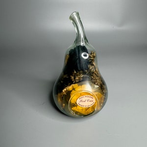 Pode incluir: Uma garrafa de vidro transparente em forma de pêra cheia de flores e ervas secas. A garrafa tem um rótulo que diz "Pot Pourri Port Cros Fabrique en Provence".