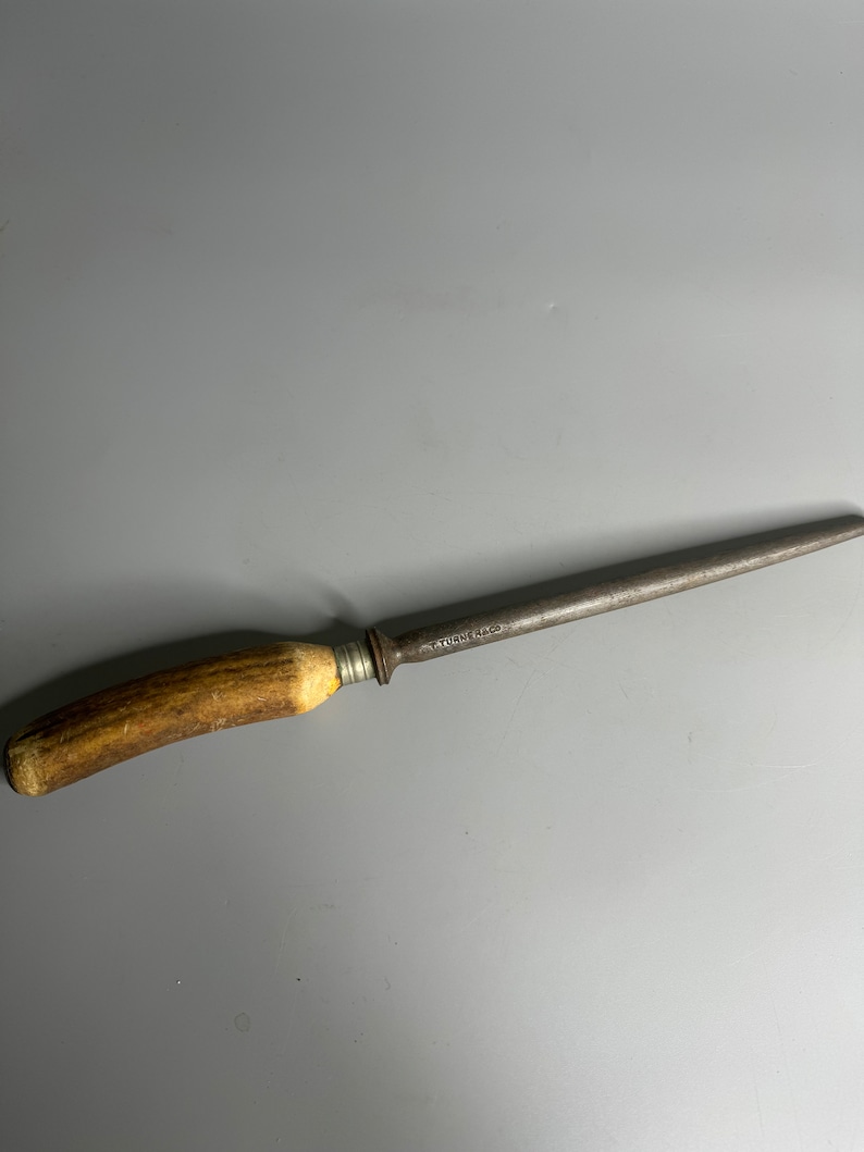 May include: A vintage steel knife sharpener with a brown antler handle. The sharpener is marked "TUSK & CO."