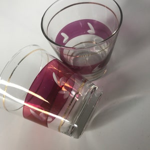 May include: Two clear glass tumblers with a gold rim and a pink band around the middle. The pink band has a white design.