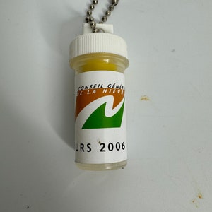 May include: A white plastic keychain with a yellow ball inside. The keychain has a green wave logo and the text "Conseil Général de la Nièvre" and "URS 2006".