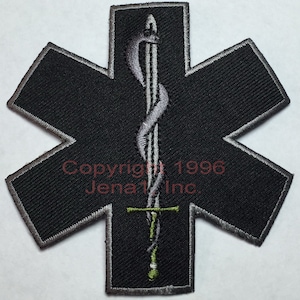 May include: Black embroidered patch with a silver star of life and a silver sword with a green handle. The text "Copyright 1996 Jena 1 Inc." is visible in the lower center of the patch.