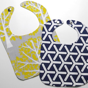 May include: Two baby bibs, one with a gray background and yellow leaf pattern, the other with a navy blue background and white geometric pattern.