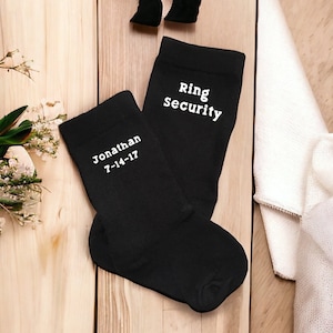 May include: A pair of black socks with white text. One sock says "Jonathan 7-14-17" and the other says "Ring Security".