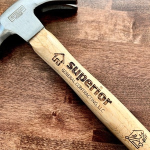 May include: A wooden-handled hammer with a black metal head. The handle is engraved with the text "Superior General Contracting, LLC" and a house icon.