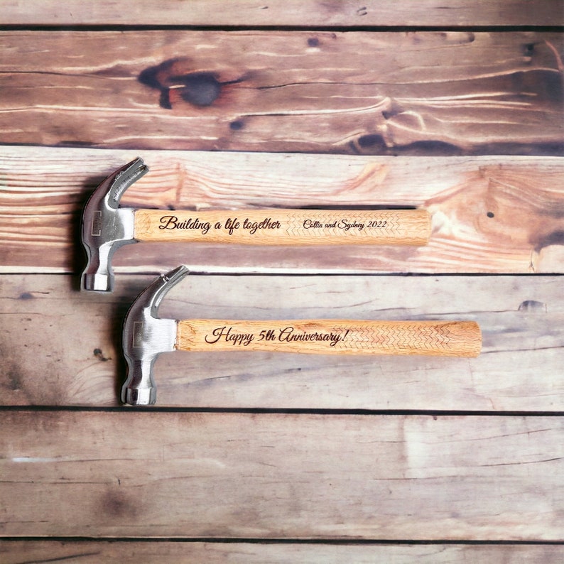 Op de afbeelding: Twee zilveren hamers met houten handvatten. De handvatten zijn gegraveerd met de tekst "Building a life together, Collie and Sydney 2022" en "Happy 5th Anniversary!"