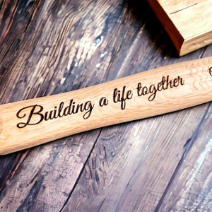 Op de afbeelding: Een houten deegroller met de woorden "Building a life together" erop gegraveerd. De deegroller ligt op een houten oppervlak.