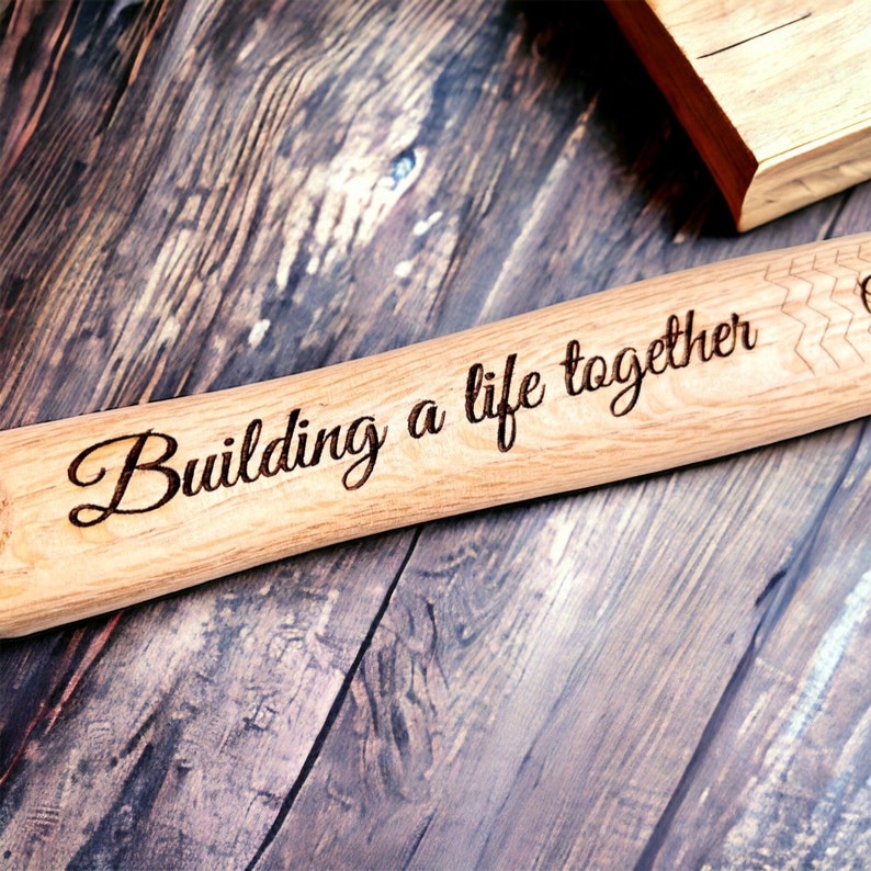 Op de afbeelding: Een houten deegroller met de woorden "Building a life together" erop gegraveerd. De deegroller ligt op een houten oppervlak.