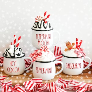May include: Four white mugs with black rims and red lettering. The mugs are filled with whipped cream and topped with candy canes, peppermint swirls, and a gingerbread man. The mugs are labeled "Hot Cocoa", "Peppermint Mocha", "Peppermint", and "Gingerbread".