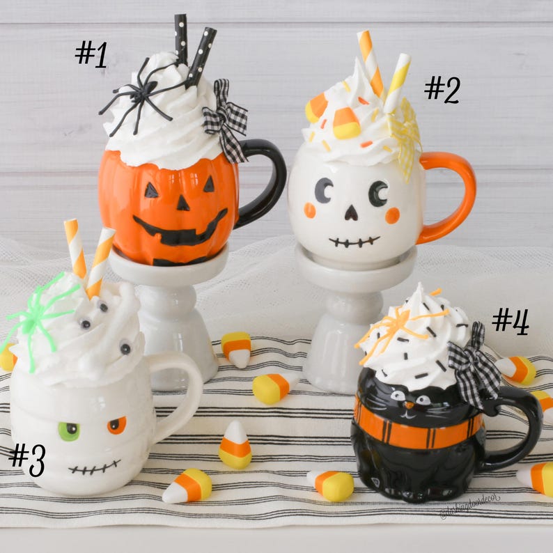 Puede incluir: Cuatro tazas tem&aacute;ticas de Halloween con coberturas de crema batida y pajitas decorativas. Las tazas tienen forma de calabaza, fantasma, momia y gato negro. Caramelos de ma&iacute;z est&aacute;n esparcidos alrededor de las tazas. Cada taza tiene un dise&ntilde;o &uacute;nico.