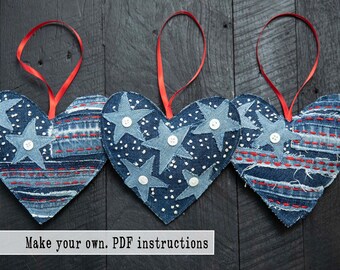 Puede incluir: Tres adornos de corazón de mezclilla con cintas rojas. Cada corazón está decorado con estrellas blancas y botones. El texto "Make your own. PDF instructions" está en la parte inferior de la imagen.