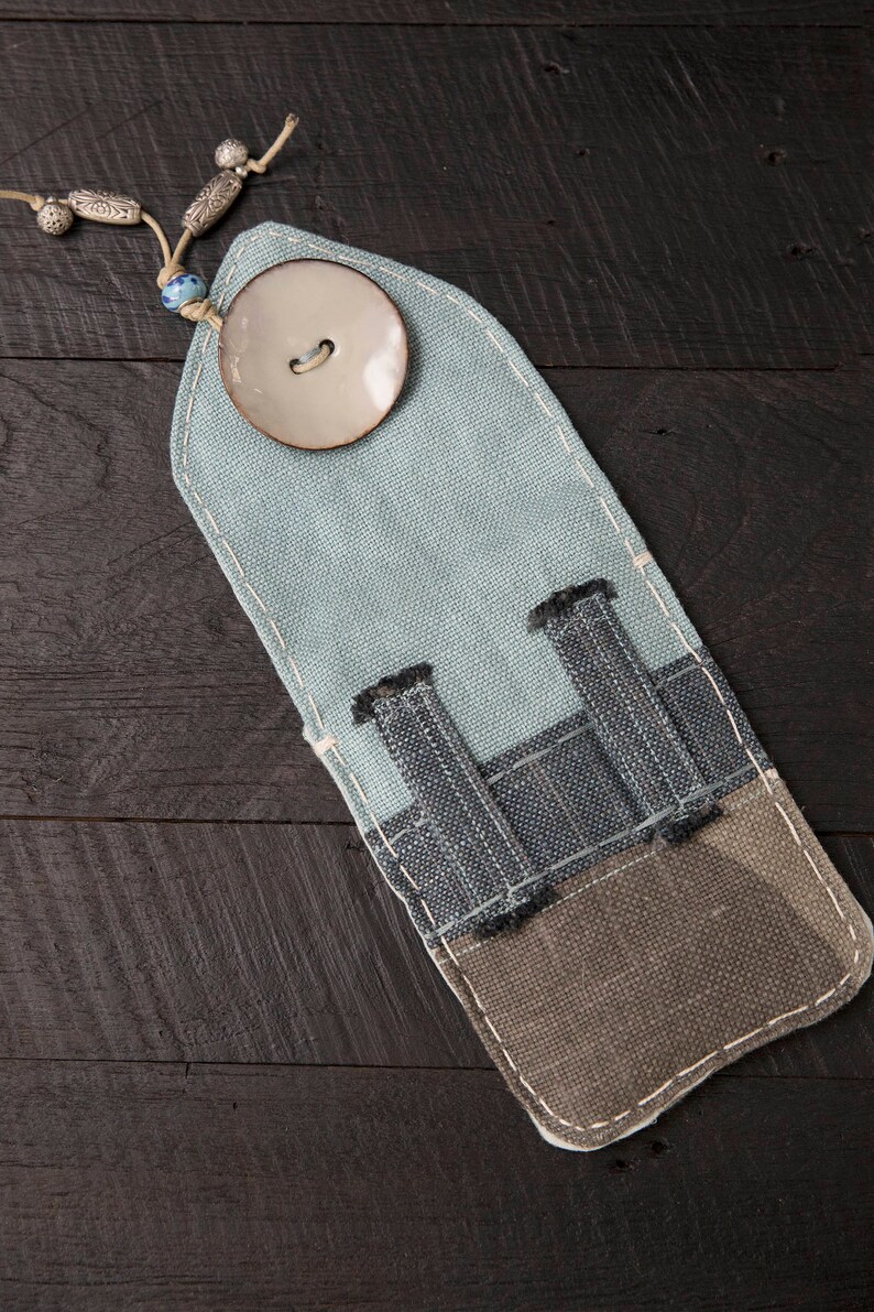 May include: A light blue fabric pencil case with a white button and three pockets. The case is made of a patchwork of different fabrics.