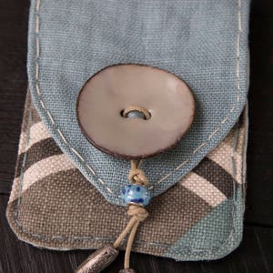 May include: A small blue and brown fabric pouch with a decorative button and a beaded tassel. The pouch has a flap that closes with the button.